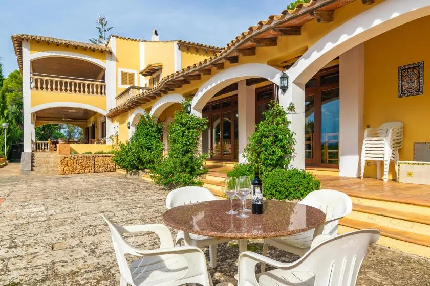 A sunny patio with a round table and white seating beside an arched building.