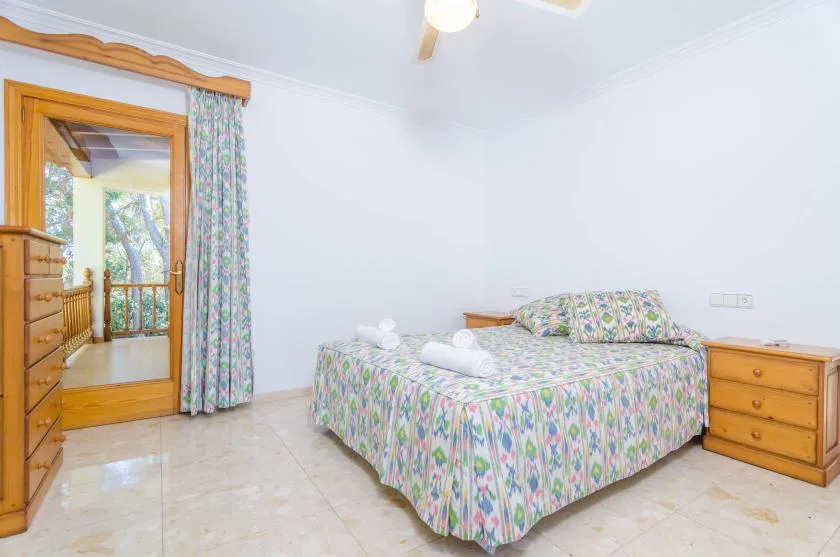 A bedroom with a floral-patterned bed and a wooden doorway opening to a balcony.