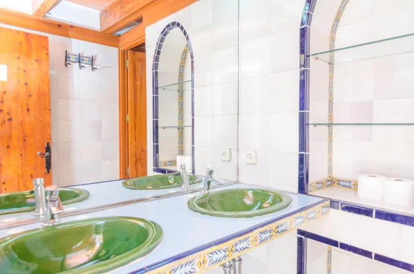 A tiled bathroom with green sinks, mirrors, and a wooden door.