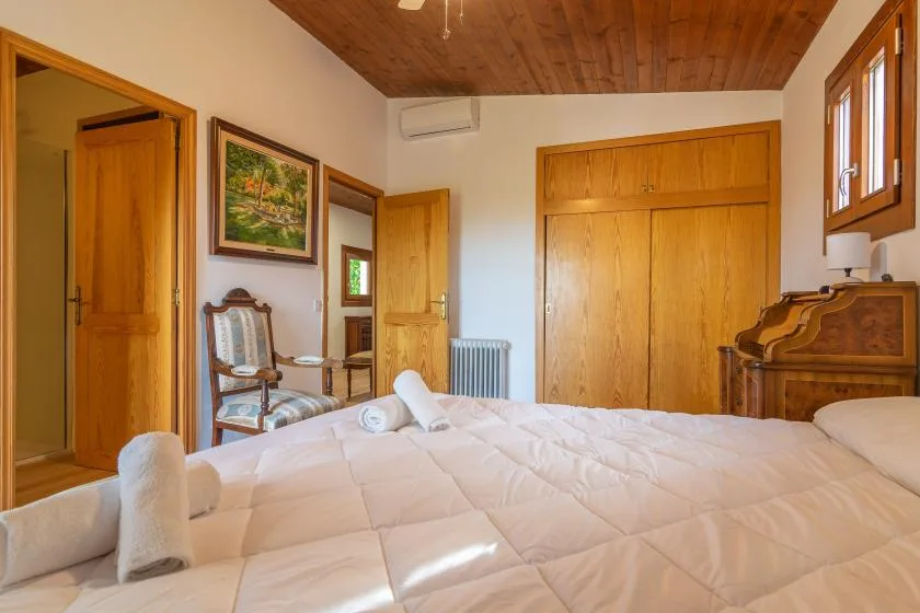 A bedroom with a wooden bed frame, bedside dresser, and pale quilted bedding.