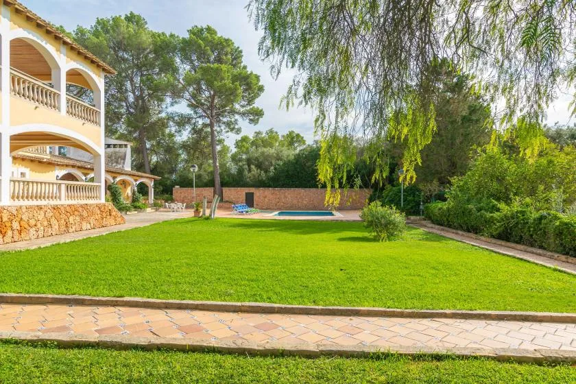 A landscaped garden lawn beside a two-story house, with trees and a swimming pool.