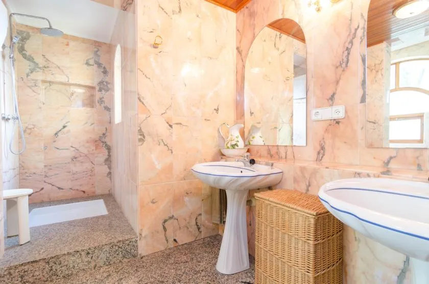 A marble-tiled bathroom with a shower, pedestal sink, and wicker basket.