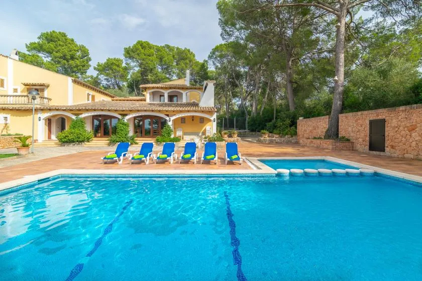 Outdoor swimming pool beside a villa, with loungers along the patio.