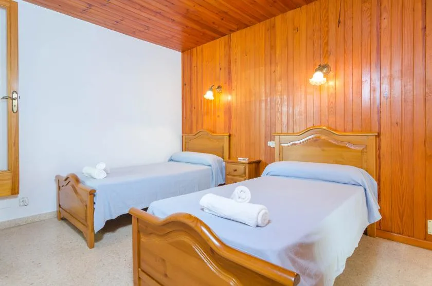 A bedroom with two beds, light bedding, and wood-paneled walls.
