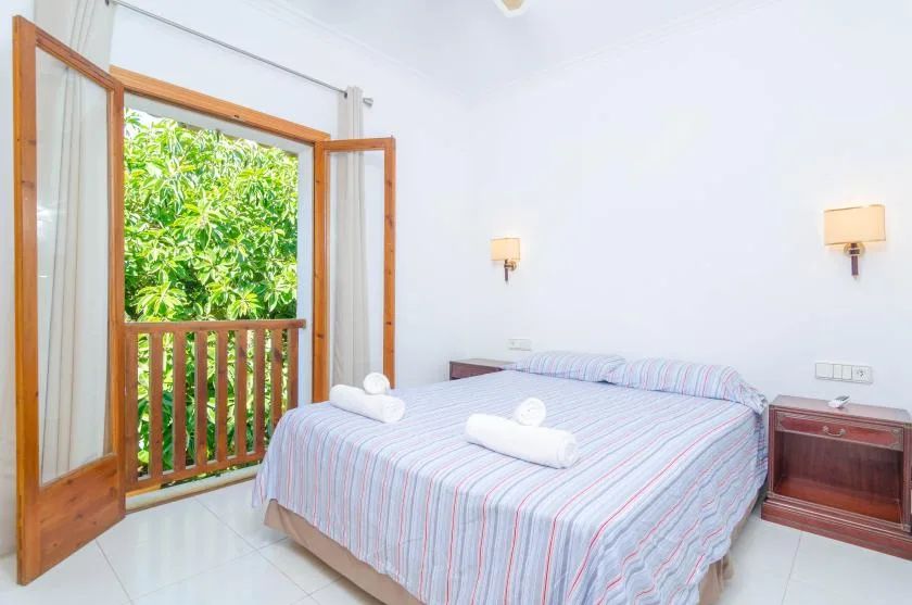 A bedroom with a striped bedspread and open wooden doors to a leafy balcony.