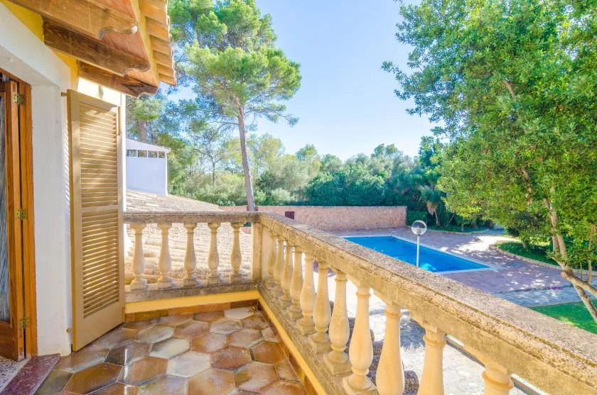 A tiled balcony overlooks a swimming pool surrounded by trees.