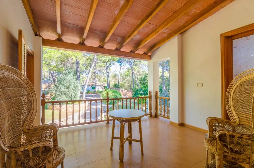 A covered balcony with woven seating and a view of trees beyond the railing.