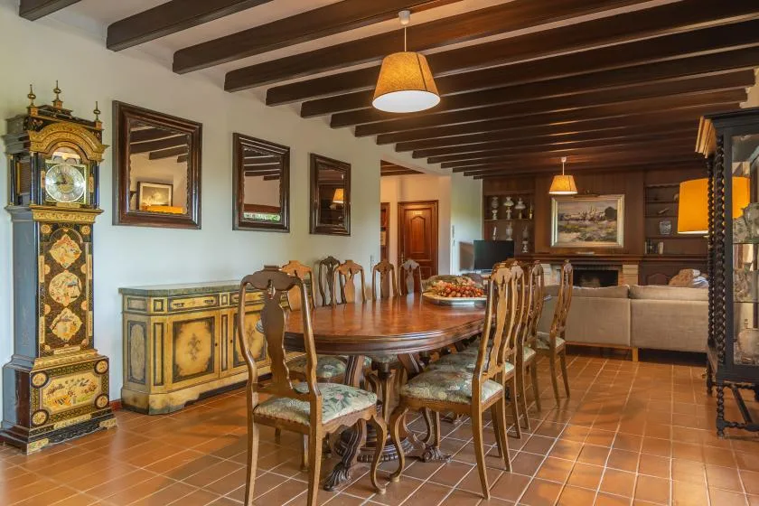 A dining room with a long wooden table and chairs beneath exposed ceiling beams.