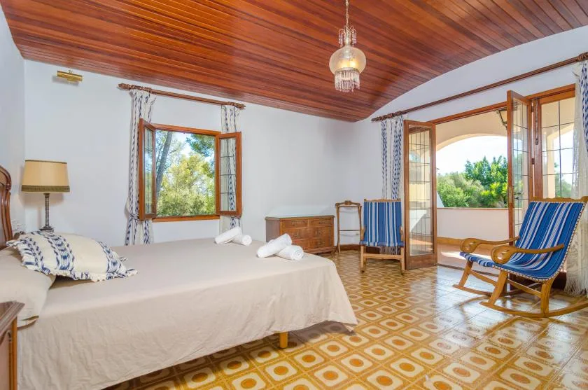 A bedroom with a bed and open doors leading to a sunlit balcony.