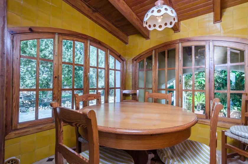 A dining area with a large wooden table beside curved windows.