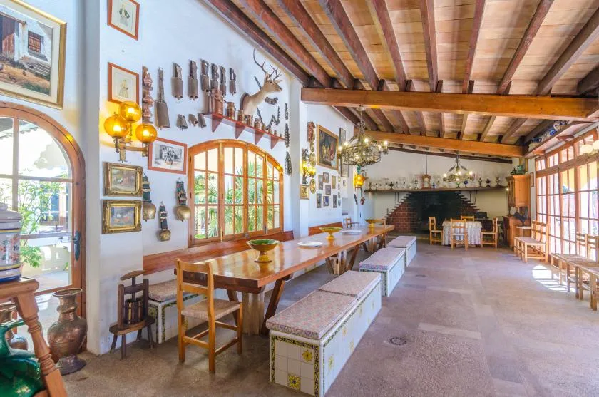 A rustic dining room with long wooden tables and benches beneath exposed ceiling beams.