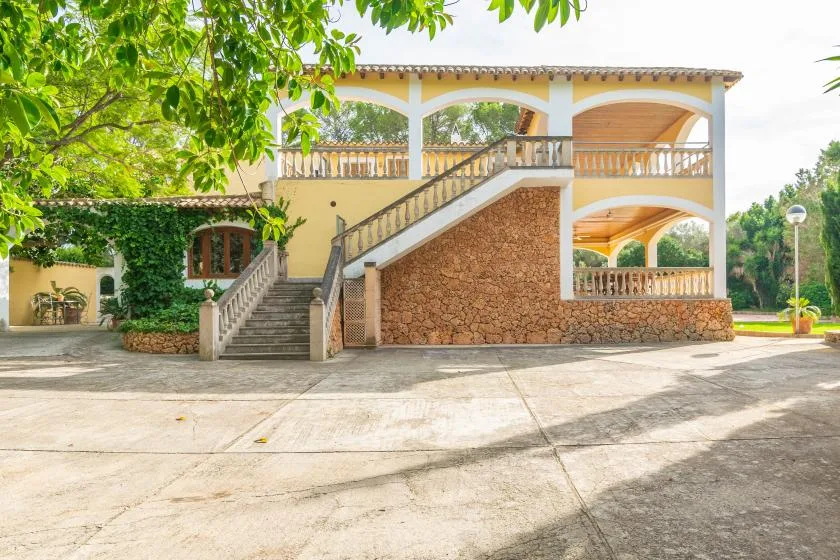 A yellow building with an exterior staircase and paved courtyard.