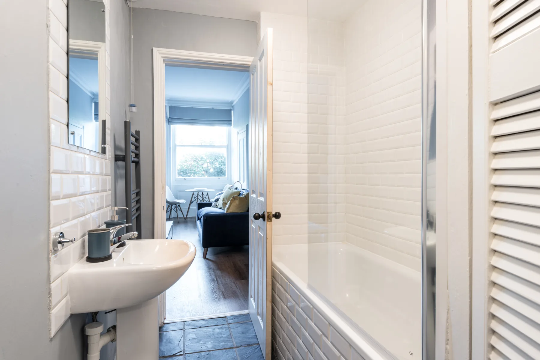 Un baño luminoso con bañera y lavabo se abre a una sala de estar.