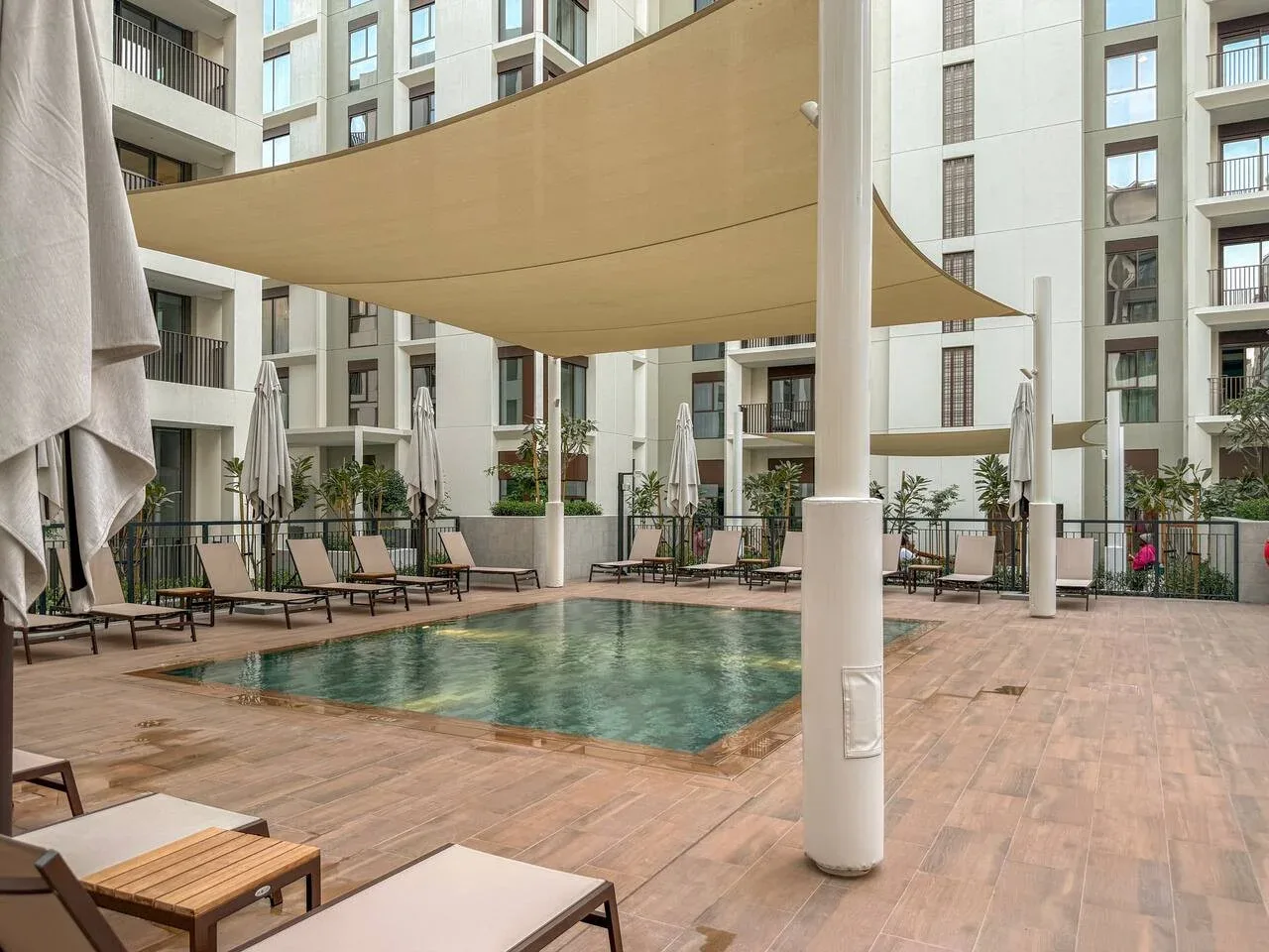 Una piscina en un patio está rodeada de asientos bajo toldos de sombra.