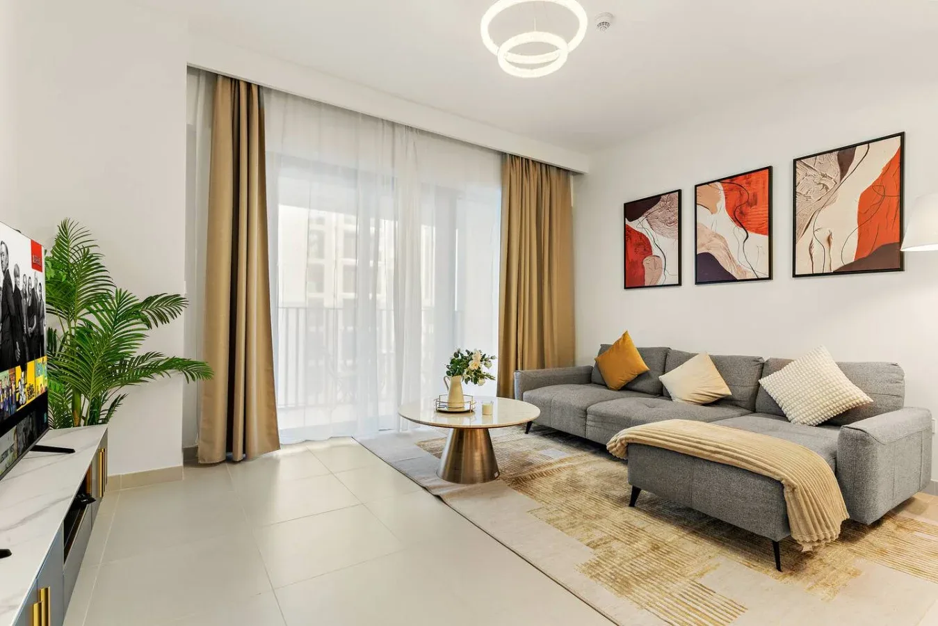 Una sala de estar con un sofá seccional gris, una mesa de centro redonda y una gran ventana con cortinas.