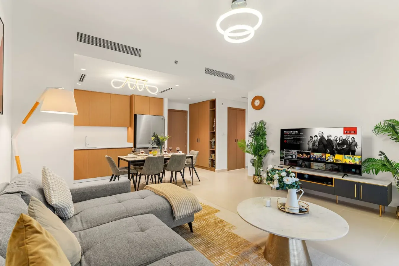 Una sala luminosa con un sofá gris, una mesa de comedor y un televisor.