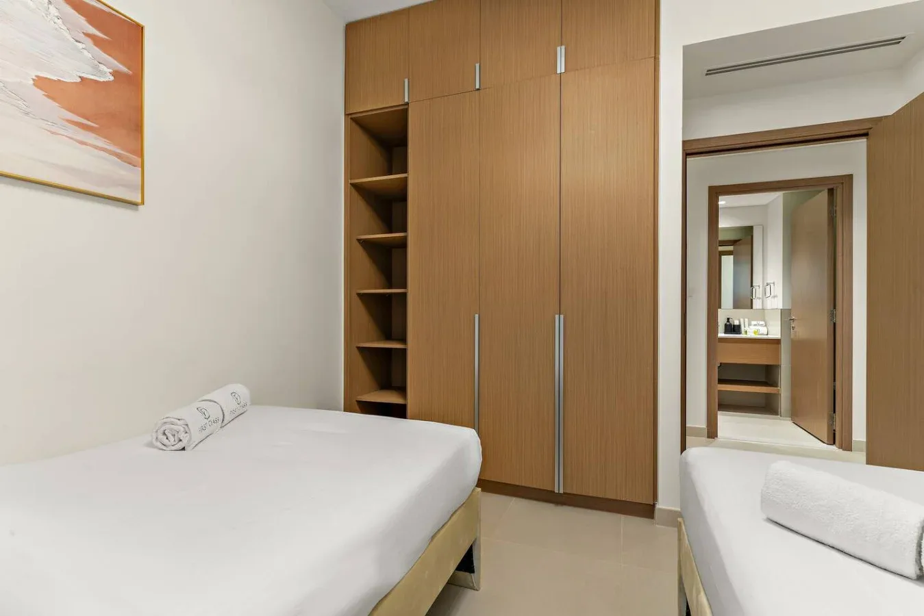 Un dormitorio con camas junto a un armario empotrado de madera y estantes abiertos.