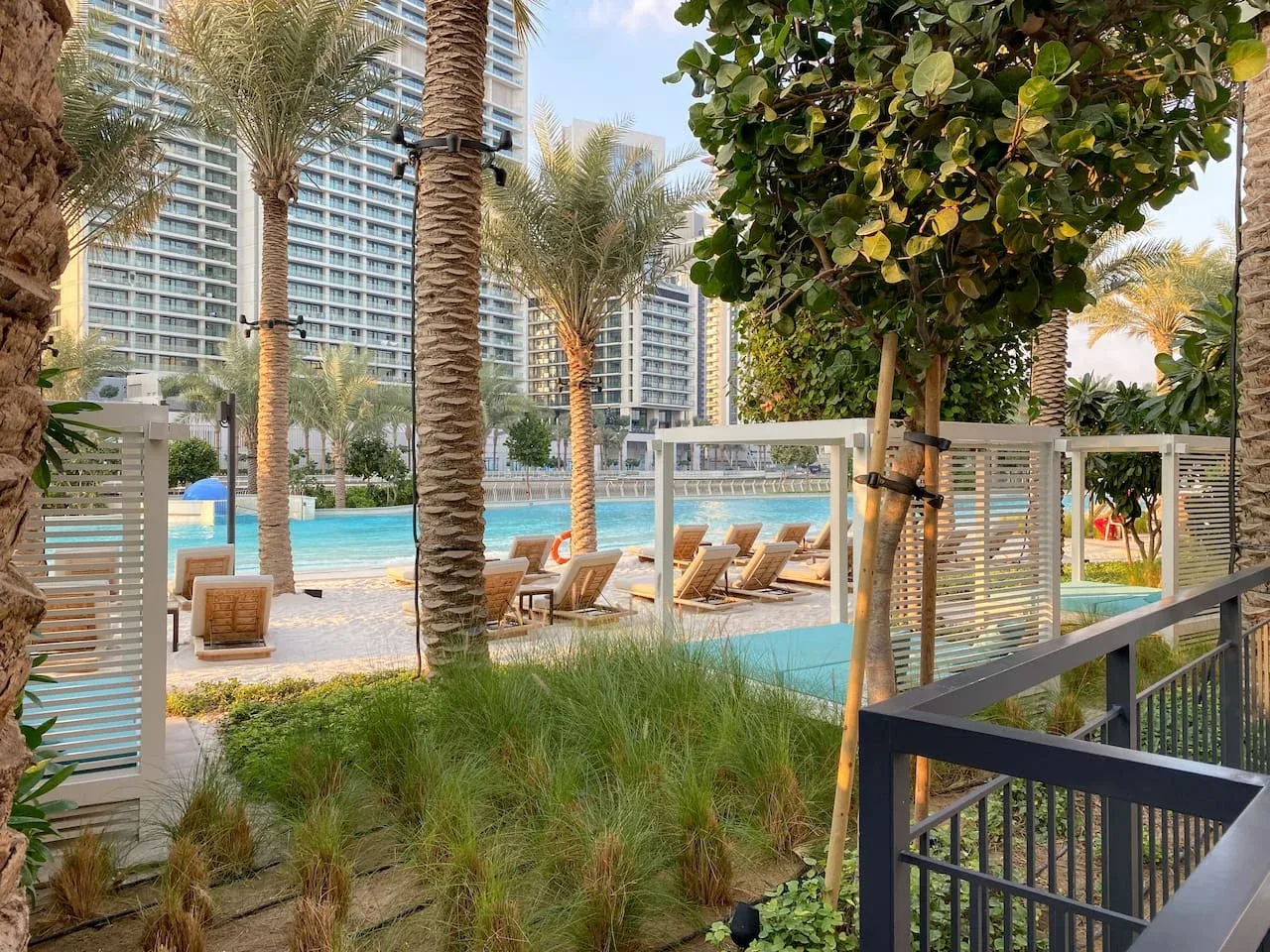 Una zona ajardinada con piscina, palmeras, asientos y edificios altos.