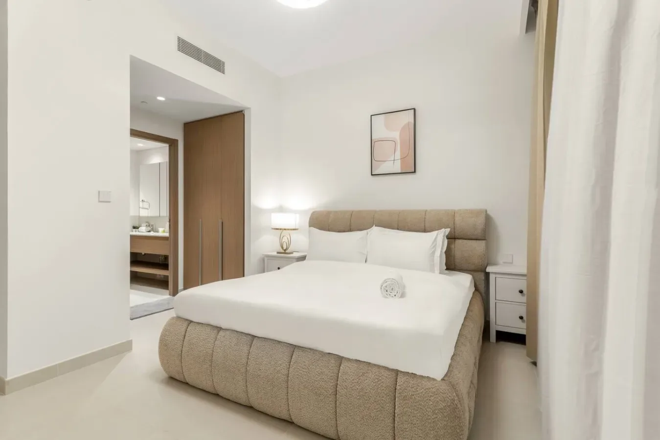 A bright bedroom with a neatly made bed and a framed picture on the wall.