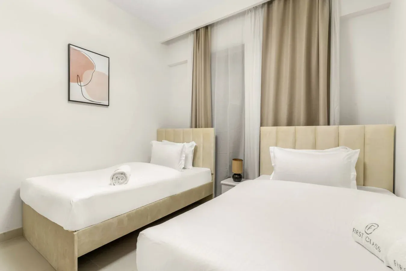 Un dormitorio luminoso con dos camas y cortinas beige.