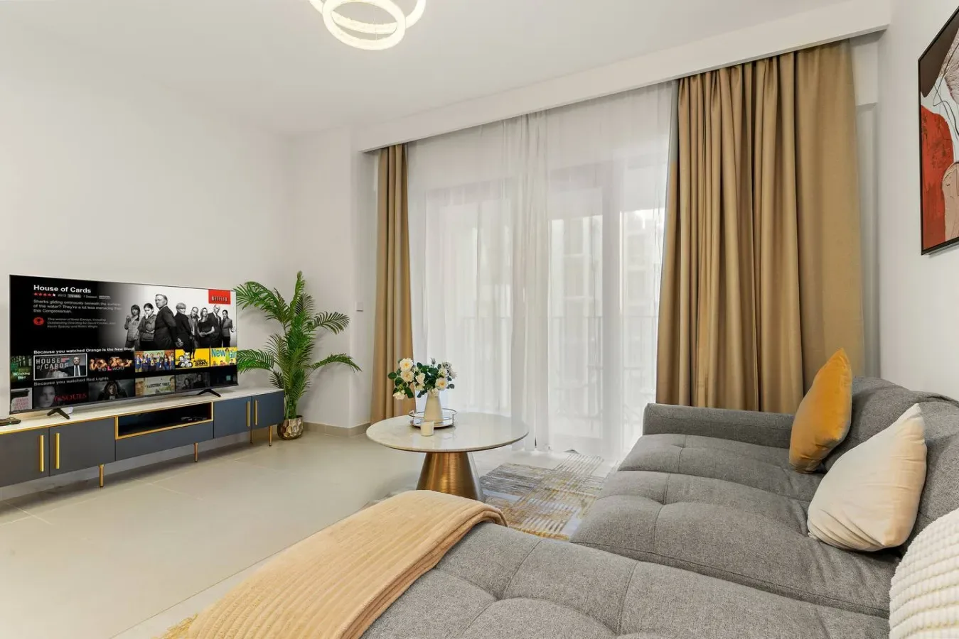 Una sala luminosa con televisor, asientos y grandes ventanas con cortinas.