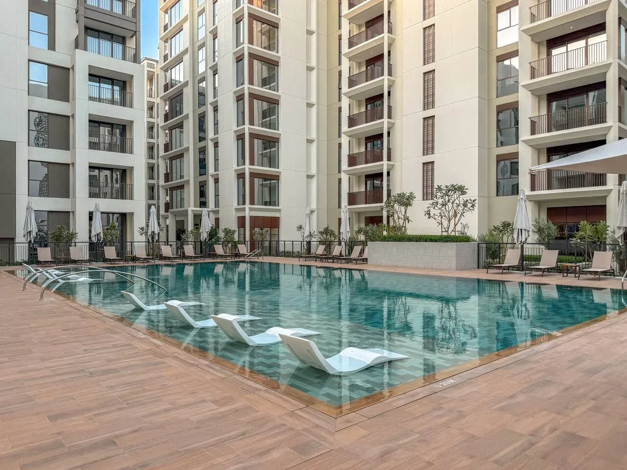 Una piscina al aire libre está junto a una terraza pavimentada y edificios de apartamentos.