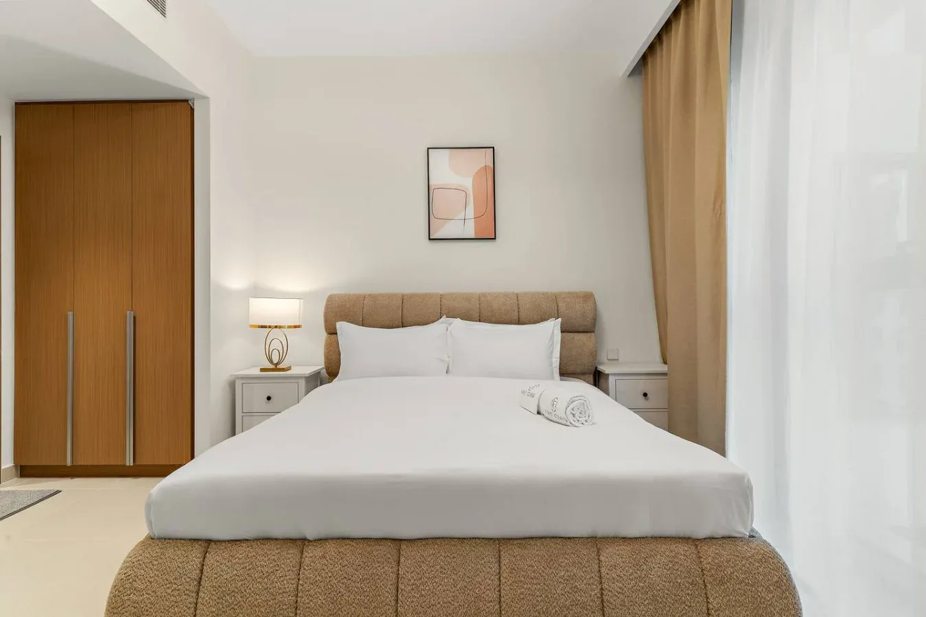 Un dormitorio con una cama bien tendida y un cuadro sobre el cabecero.