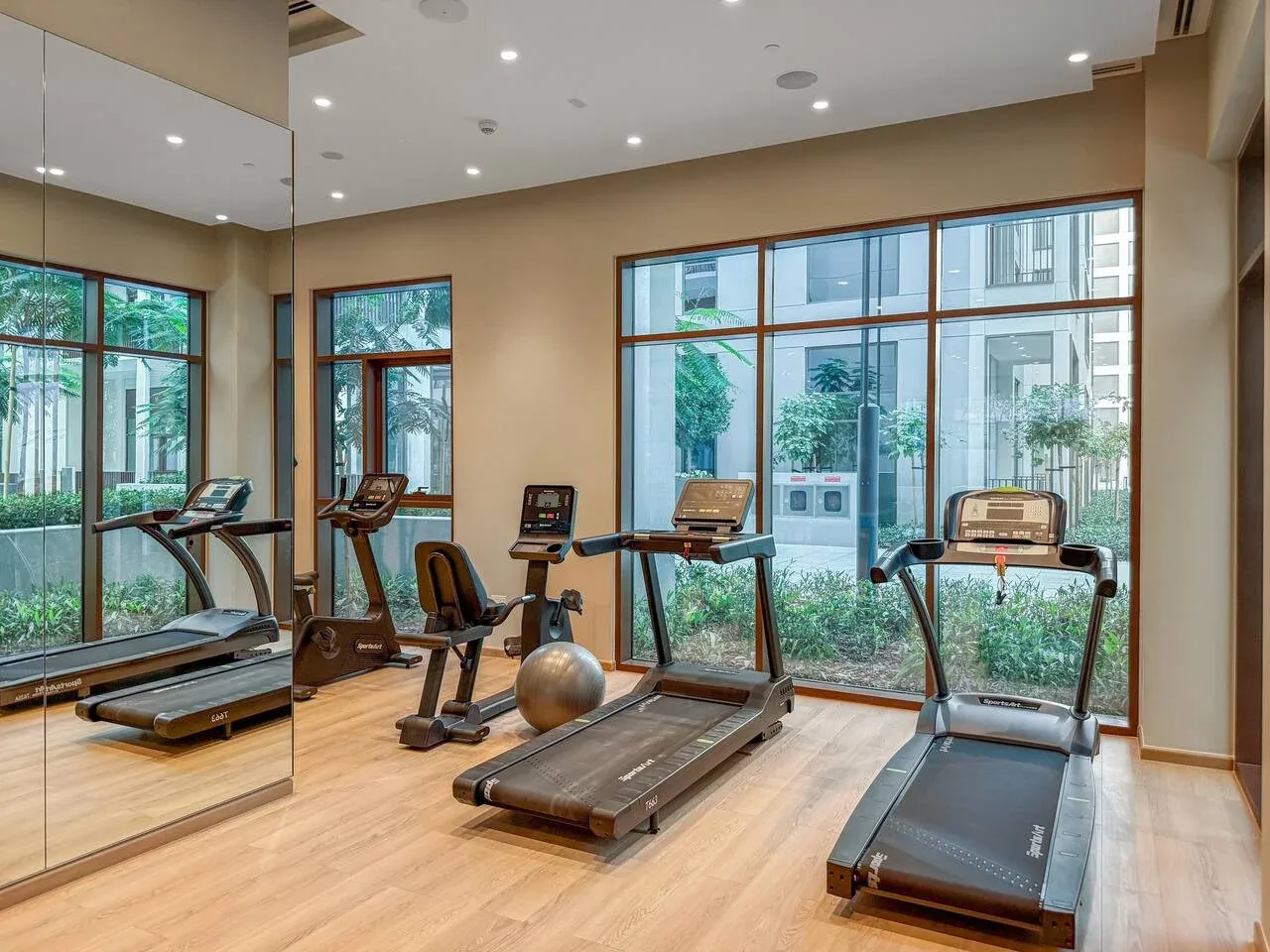 Sala de ejercicio con cintas de correr y equipo junto a grandes ventanas.