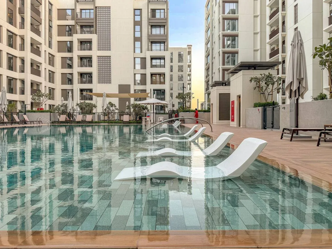 Una piscina con tumbonas sumergidas está rodeada de edificios de apartamentos modernos.