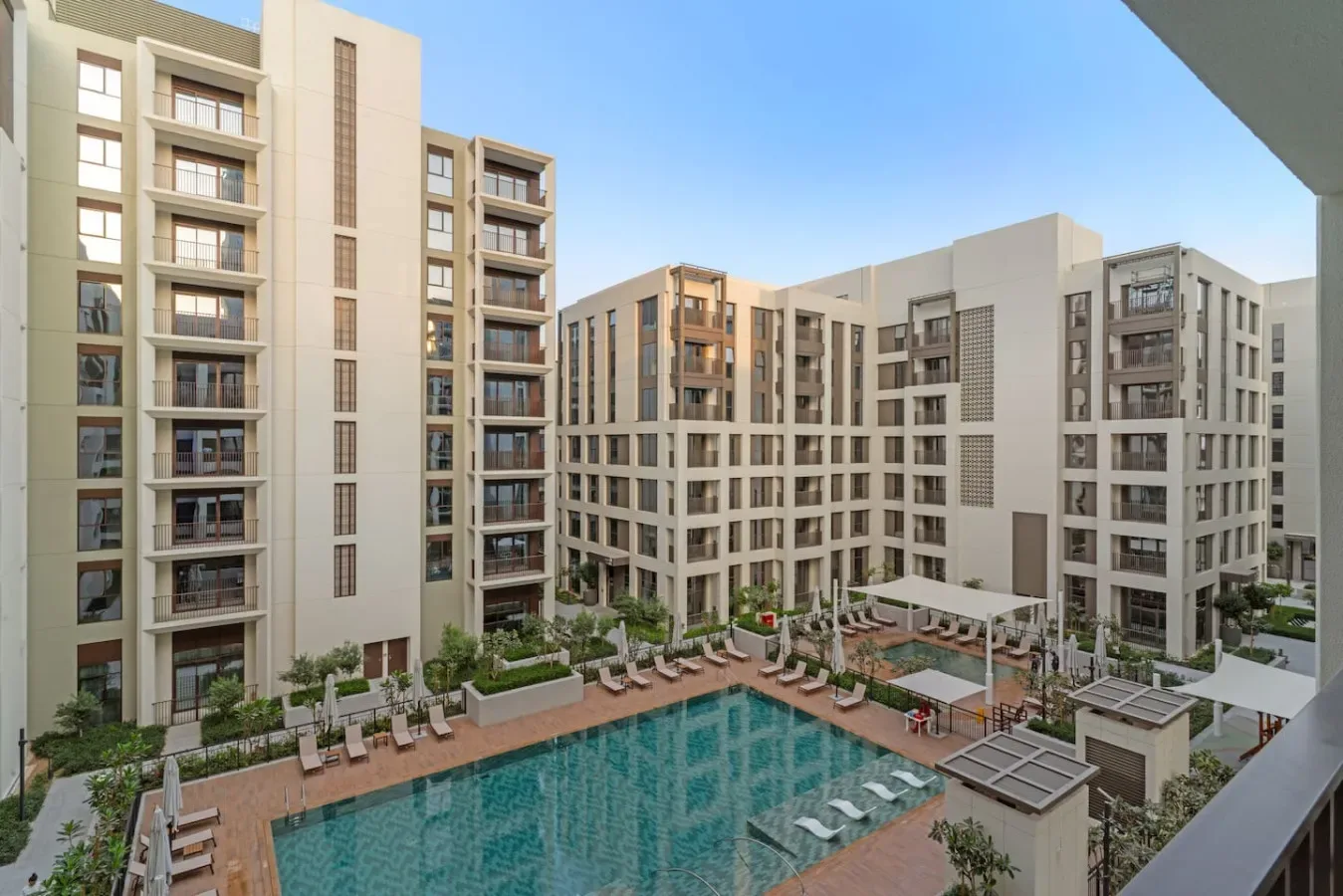 A courtyard pool sits among multi-story residential buildings and landscaped seating areas.