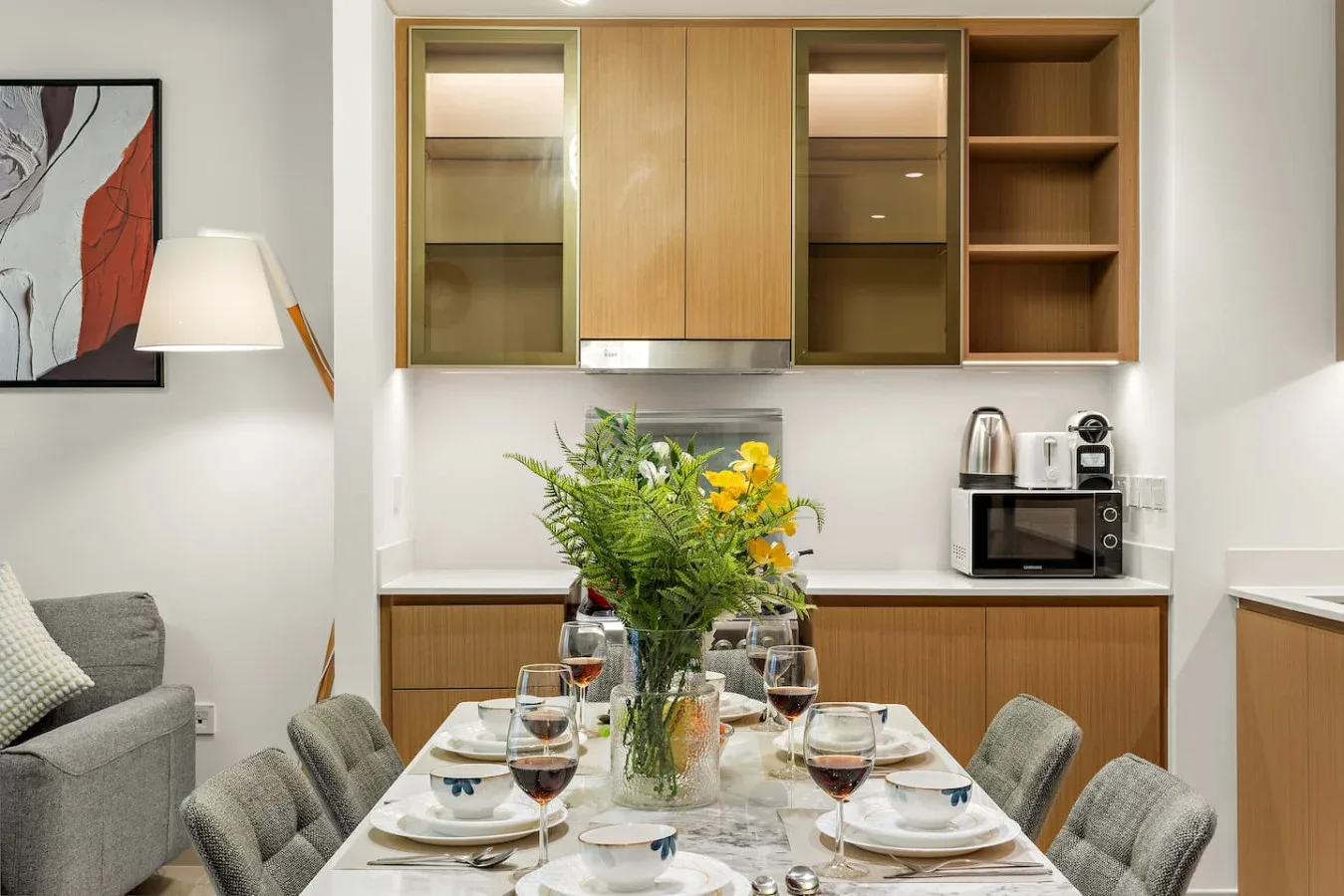 Un comedor preparado para una comida está junto a una cocina compacta con armarios de madera.