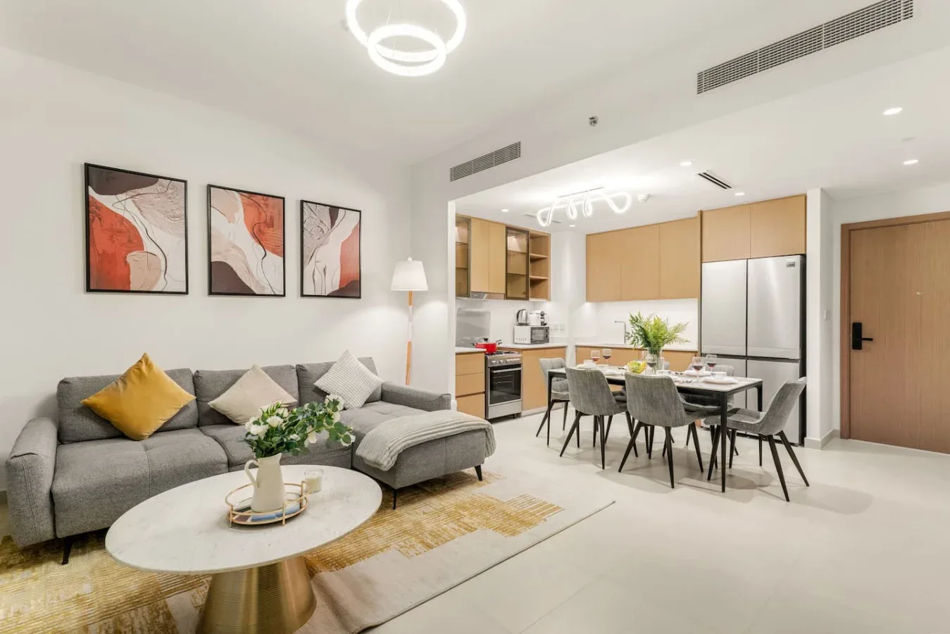 Una sala de estar y comedor modernos se abre a una cocina, con una zona de asientos gris.