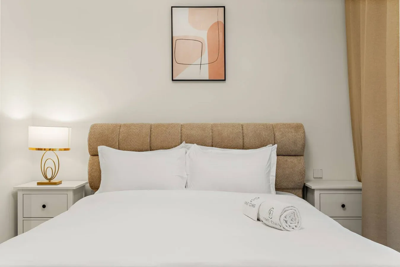 Dormitorio con una cama tendida, mesitas de noche y una lámina enmarcada.