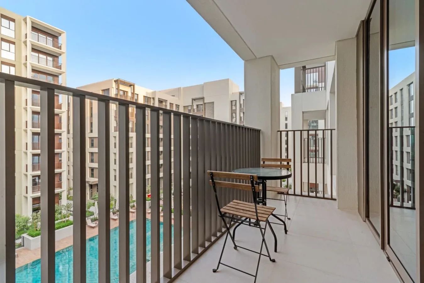 Un balcón con una mesa pequeña y asientos da a edificios de apartamentos cercanos.