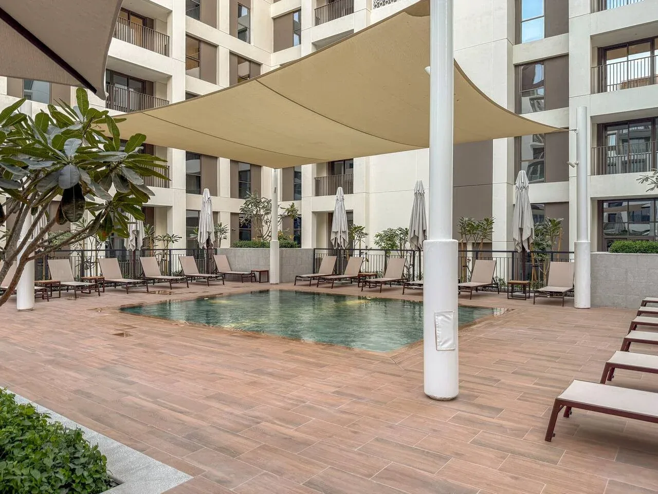 Una piscina al aire libre junto a una terraza de baldosas, asientos reclinables y toldos.