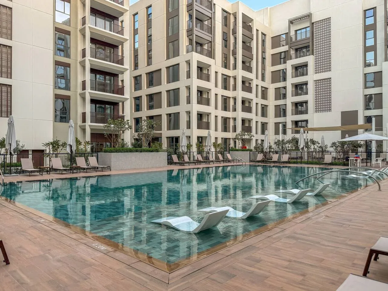 Una piscina al aire libre junto a un edificio de varias plantas, con asientos alrededor de la terraza.