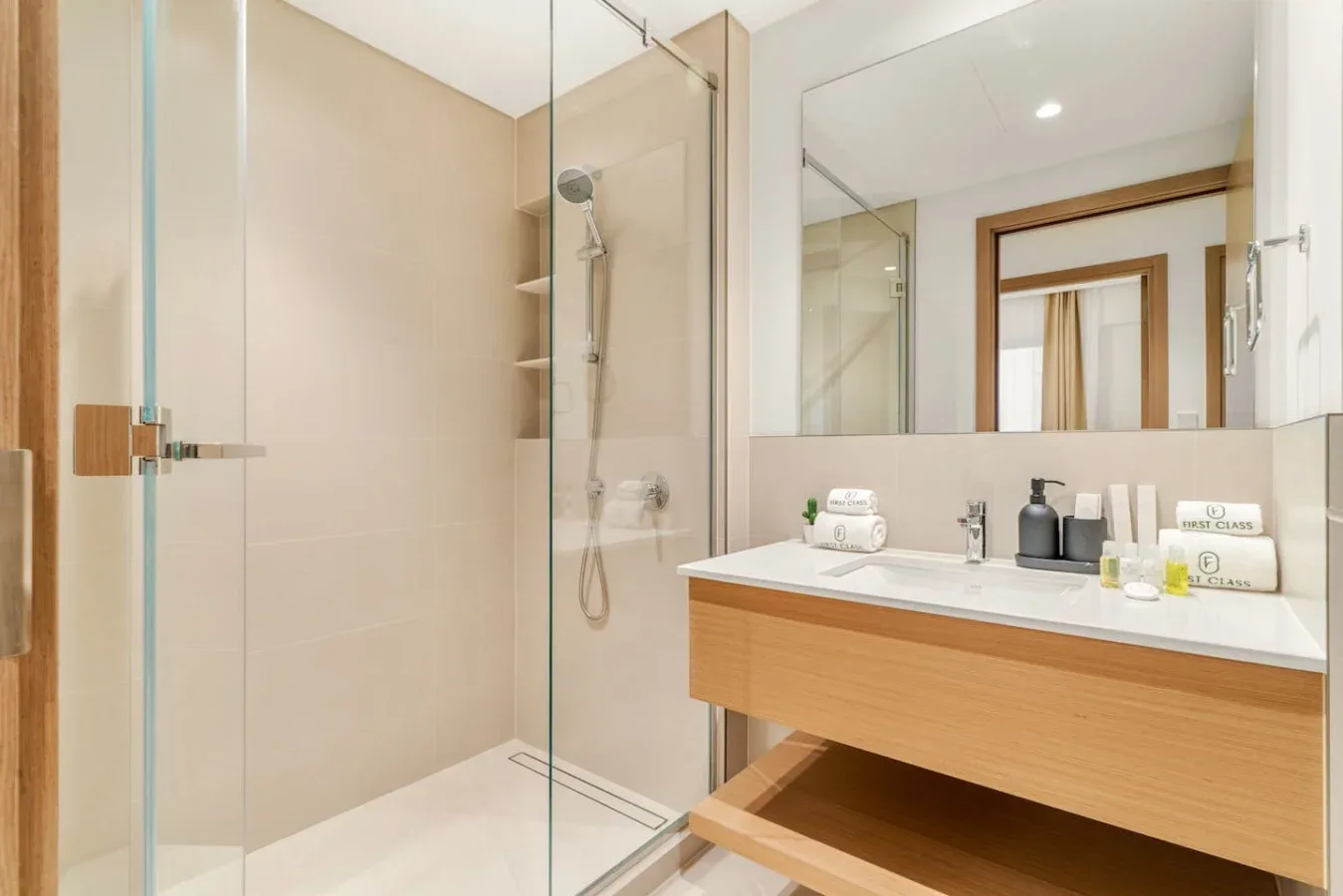 Un baño luminoso con una ducha de vidrio y un amplio lavabo bajo un espejo.