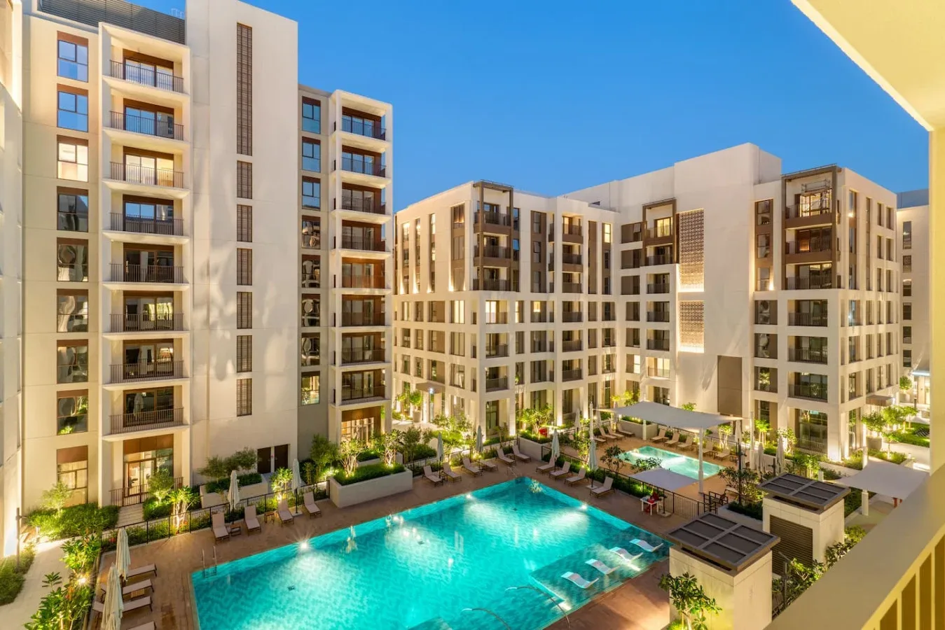 Una piscina está en un patio ajardinado rodeado de edificios de apartamentos.