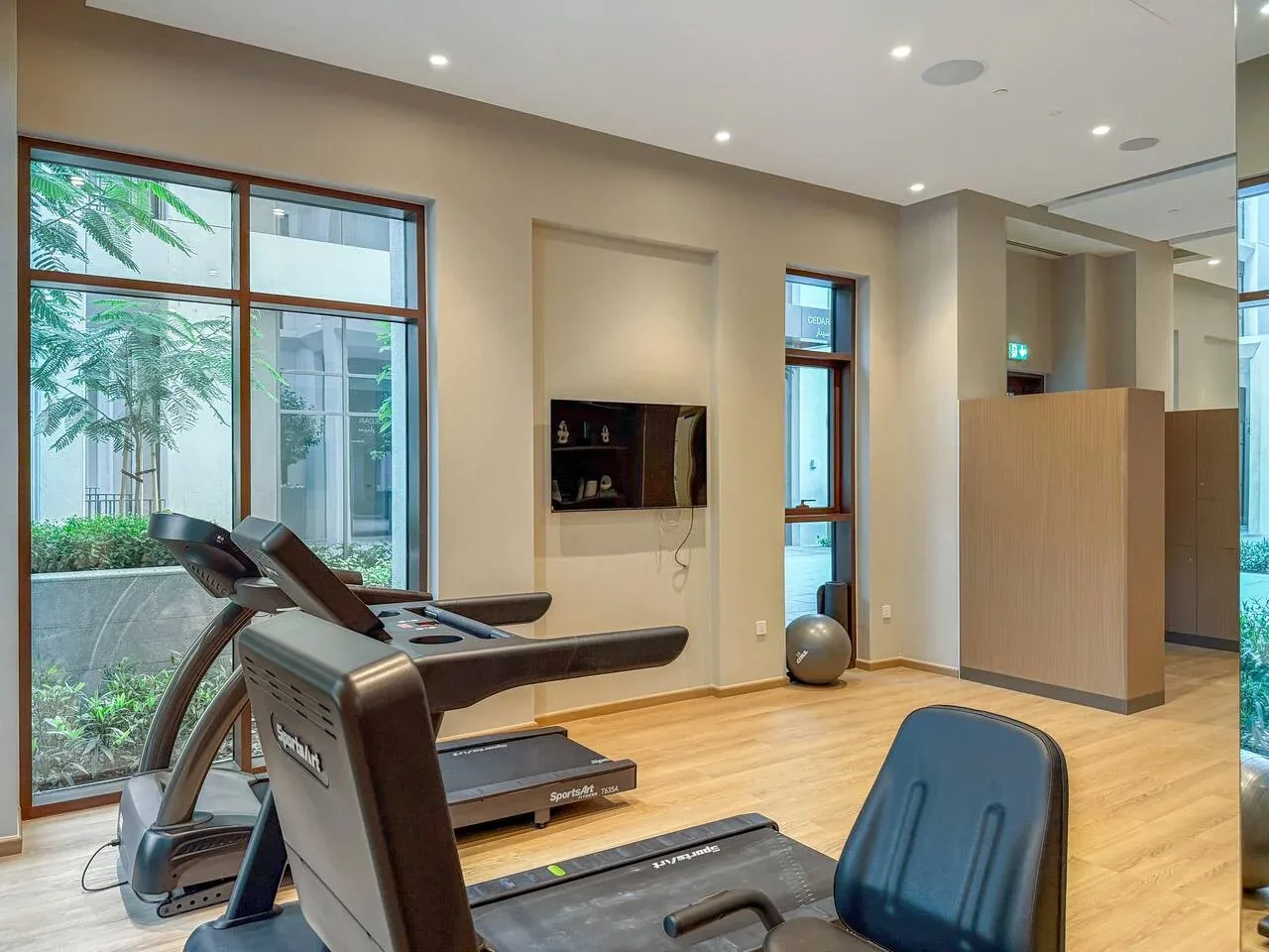 Un gimnasio con equipos de ejercicio y grandes ventanas con vistas a la vegetación.