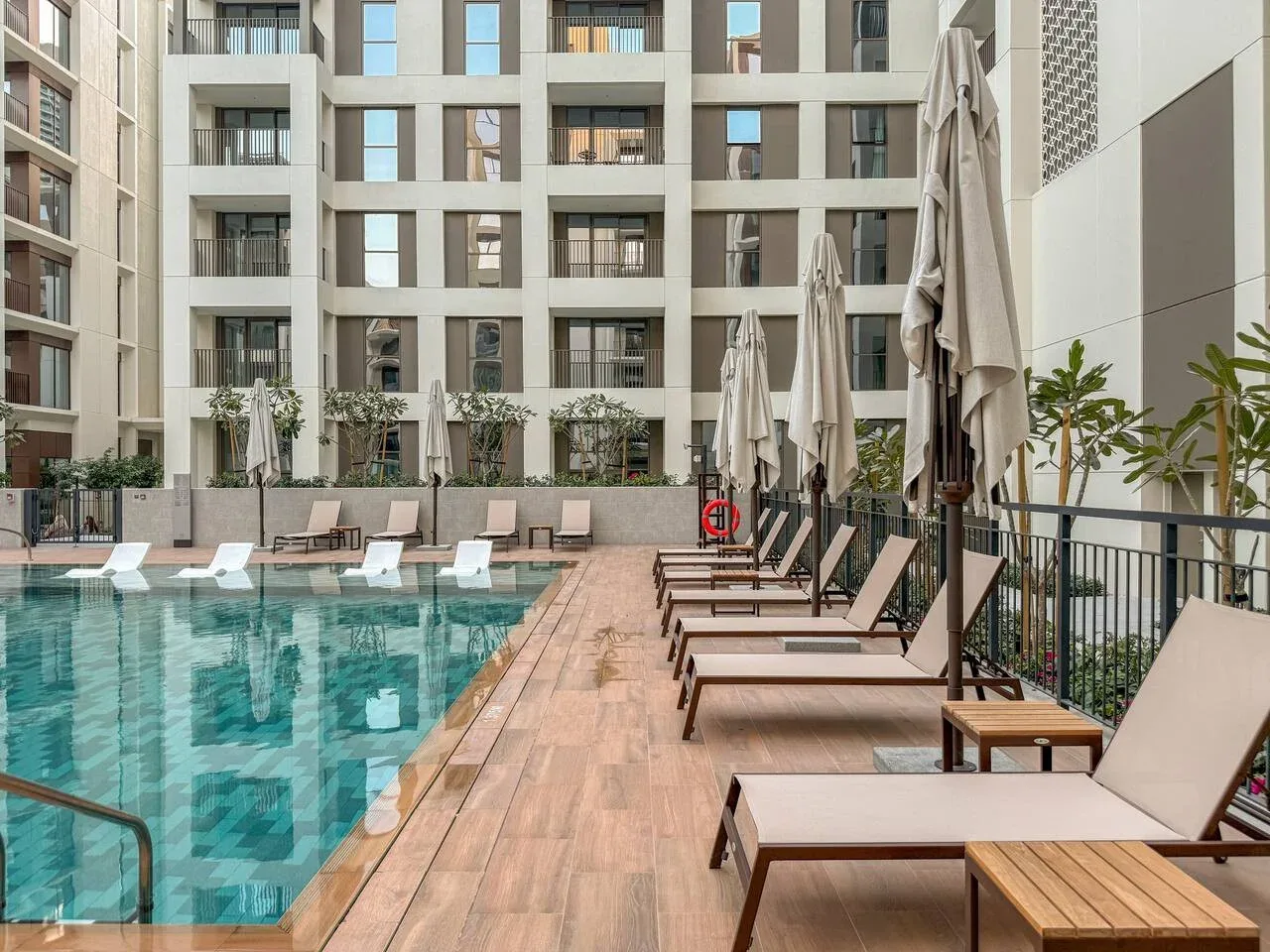 Una piscina al aire libre está rodeada de tumbonas y sombrillas cerradas.