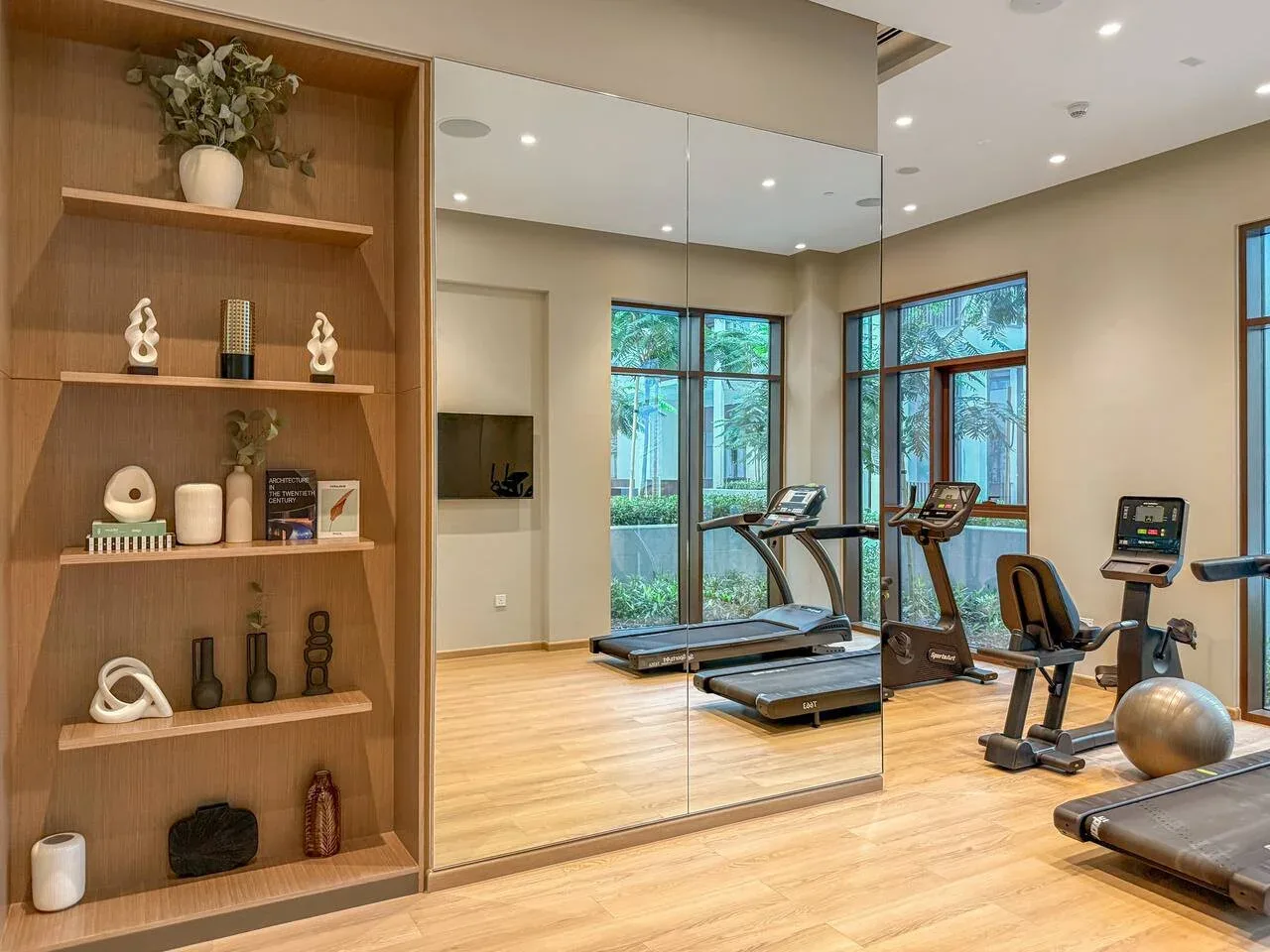 Un gimnasio luminoso con máquinas de ejercicio, paredes espejadas y grandes ventanas.