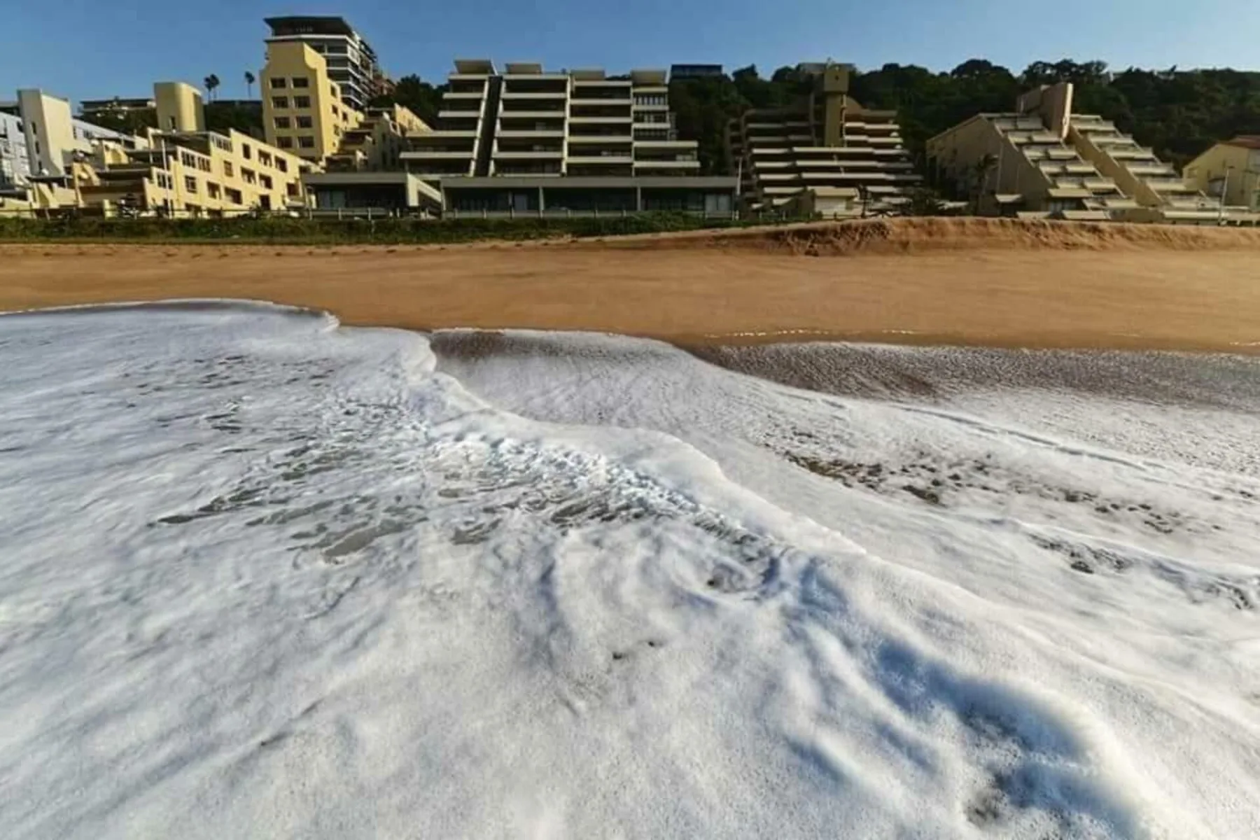 A sandy beach with foamy waves in front of beachfront buildings.