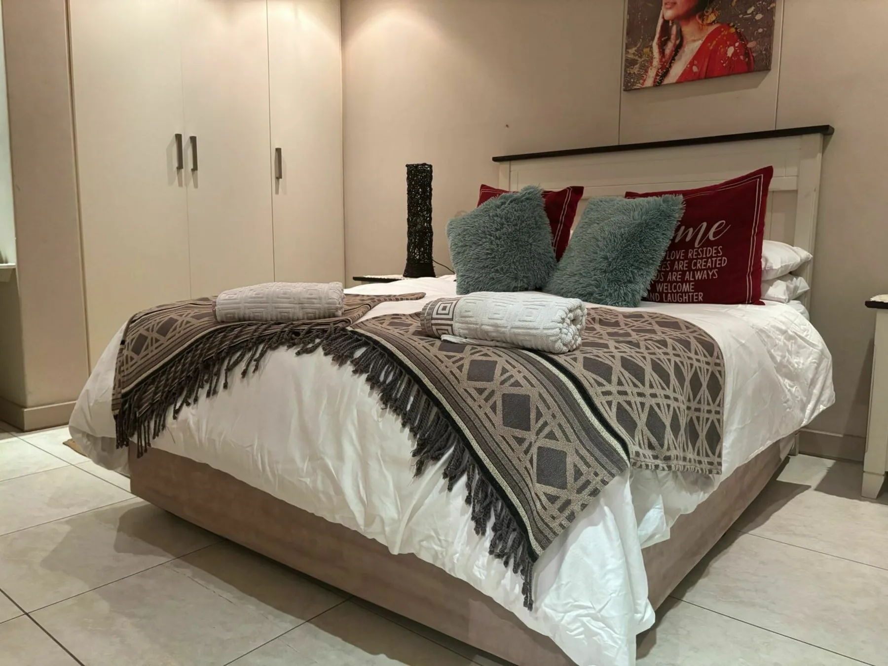 Dormitorio con una cama tendida, una manta estampada y cojines decorativos.