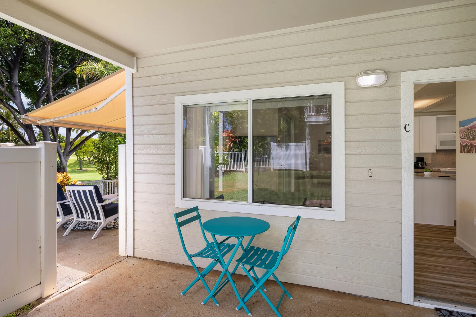 Un patio cubierto con una mesa turquesa y sillas plegables junto a una ventana.
