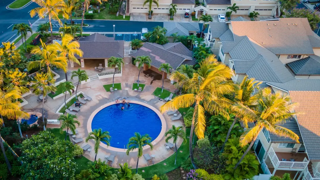 Vista aérea de una piscina de un complejo, rodeada de palmeras y edificios.