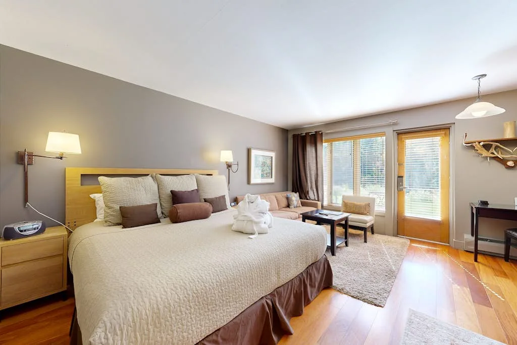 A bright bedroom with a large bed, seating area, and windows opening onto a balcony.