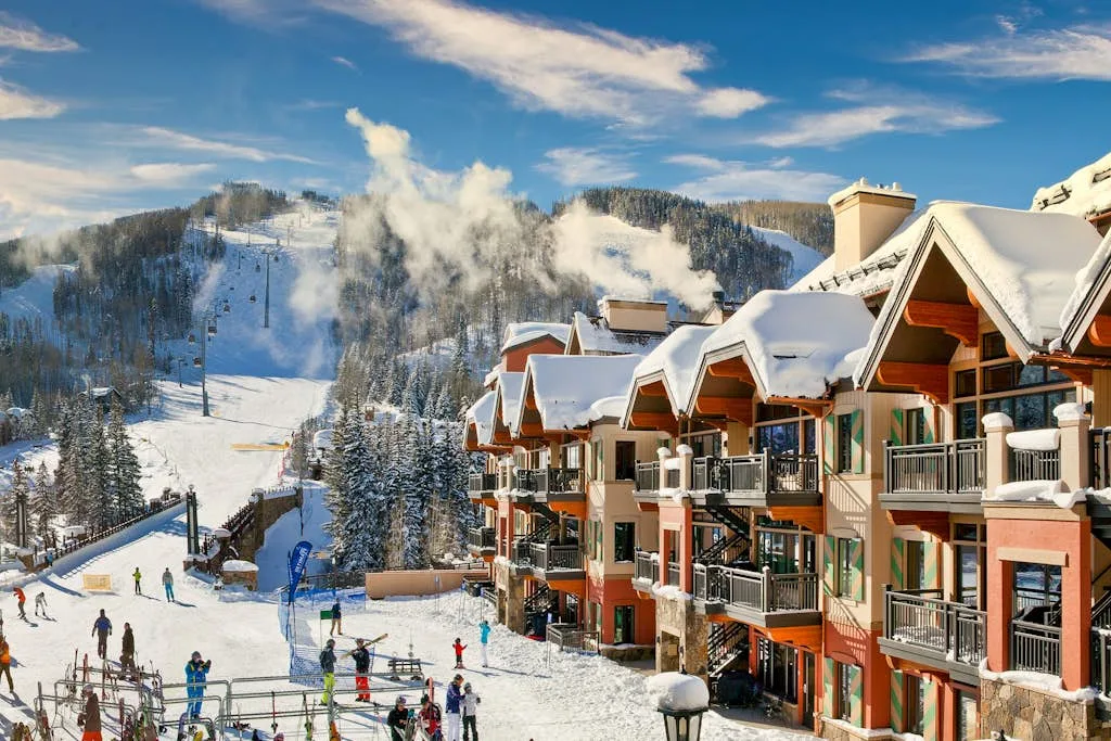Snow-covered mountain lodges overlook a ski slope with skiers.