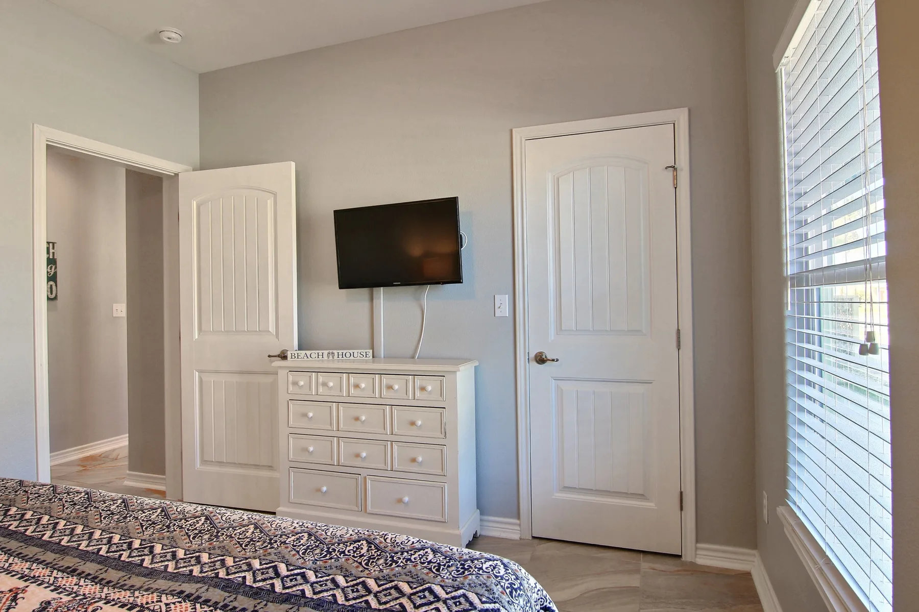 A bedroom with a television mounted above a dresser and a patterned bedspread.