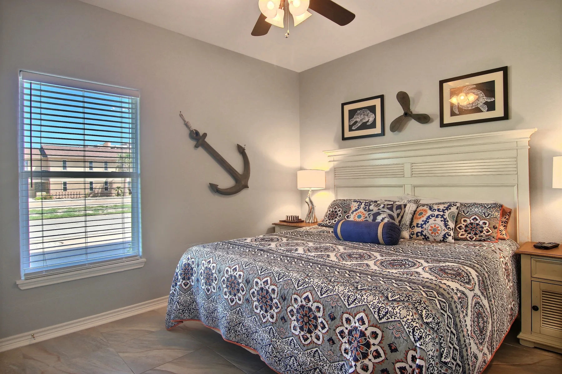 A bedroom with patterned bedding, a window with blinds, and wall decorations.