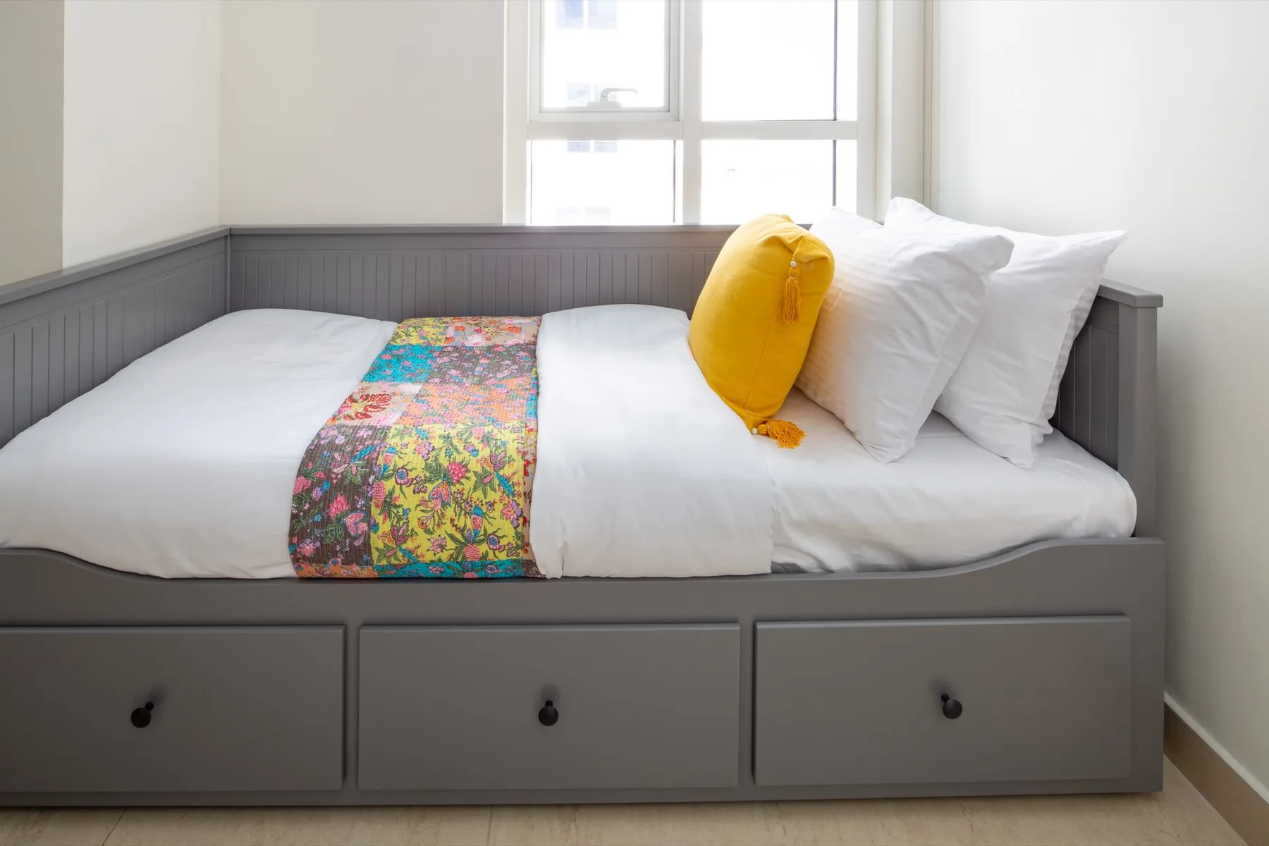 A neatly made bed with white bedding and a colorful patterned runner.